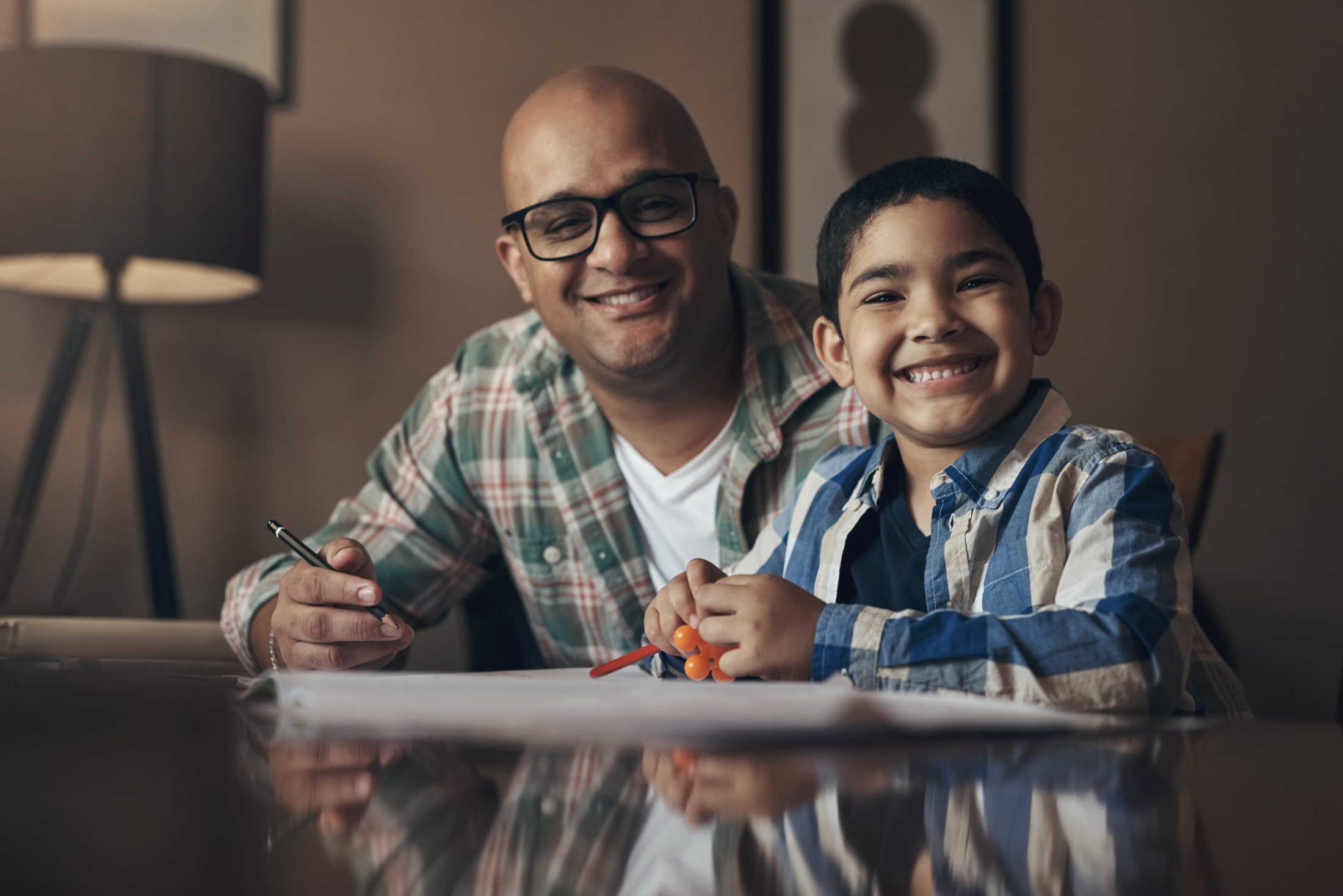 A father and son sitting together at a table, smiling at the camera.